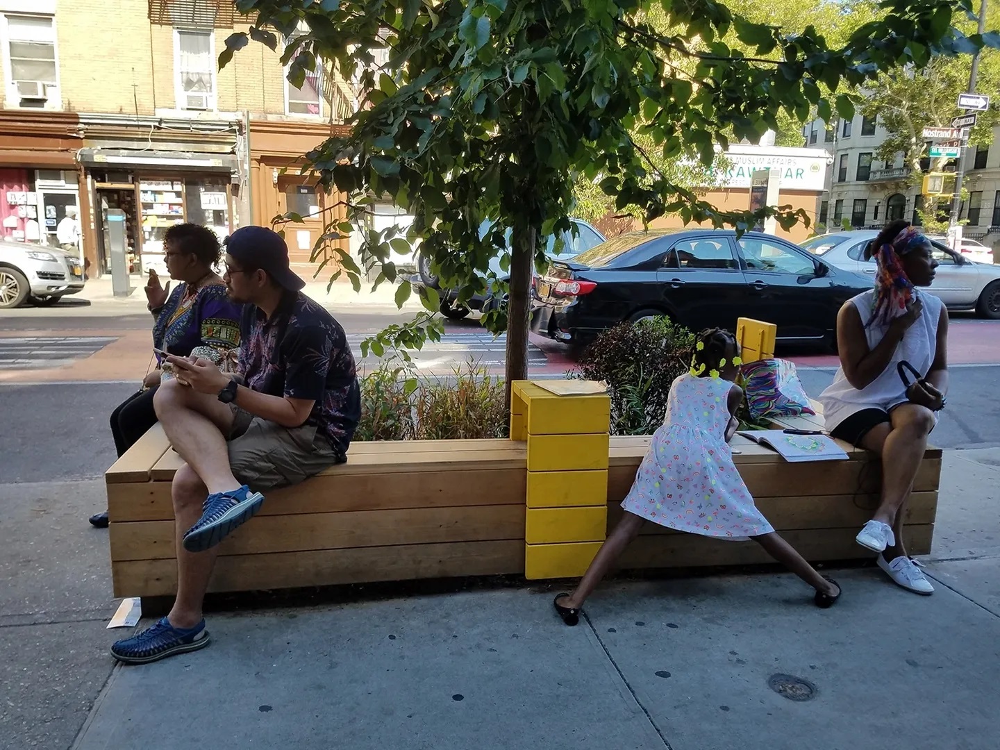 People sitting on a street side along with a tree